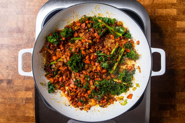 aromatics, kale, and spices cooking in a white skillet.