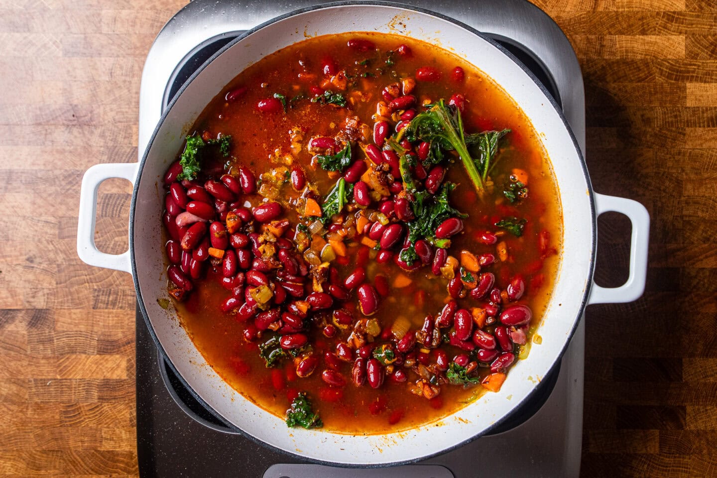 red beans, kale and aromatics cooking in white skillet.