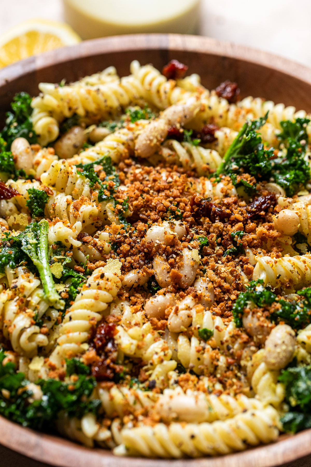close up of a roasted garlic and lemon white bean caesar pasta salad in a wooden bowl.