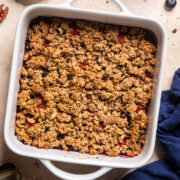 a mixed berry crumble in a white, square baking dish with handles on a table.