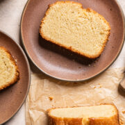 a slice of vegan pound cake on a brown plate next to a loaf of cut cake.