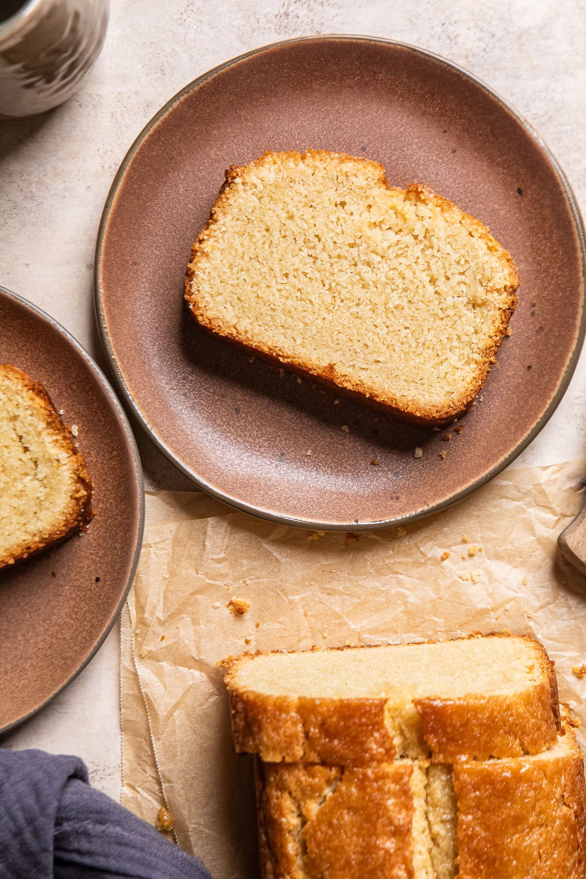 a slice of vegan pound cake on a brown plate next to a loaf of cut cake.