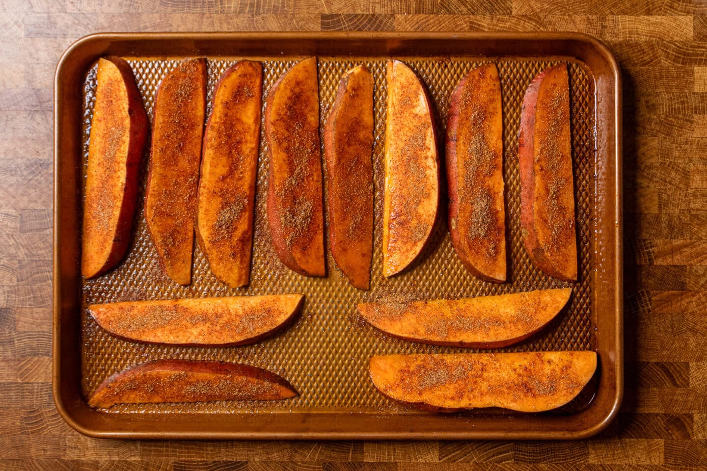 uncooked seasoned sweet potatoes on a baking tray.