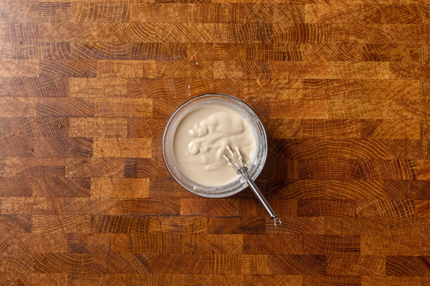 tahini butter sauce in a small glass bowl with a small whisk inside.