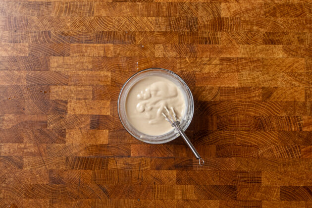 tahini butter sauce in a small glass bowl with a small whisk inside.