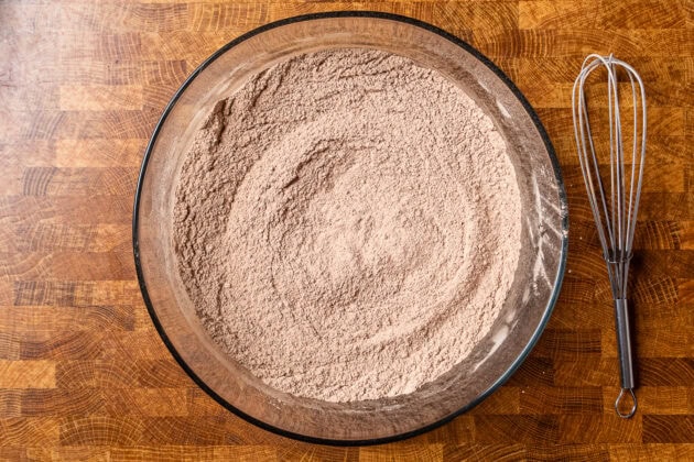 dry ingredients for chocolate cake whisked together in a glass bowl on a table.