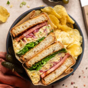 a crispy lemon dill pickle chickpea salad sandwich with lettuce and tomatoes split in half sitting in a bowl.