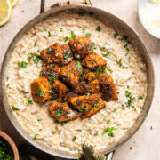 vegan chicken alfredo orzo in a stainless steel skillet with crispy tofu "chicken" on top.