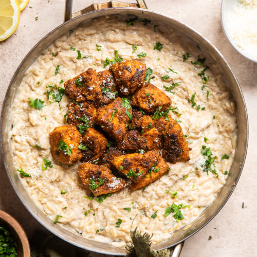 vegan chicken alfredo orzo in a stainless steel skillet with crispy tofu "chicken" on top.