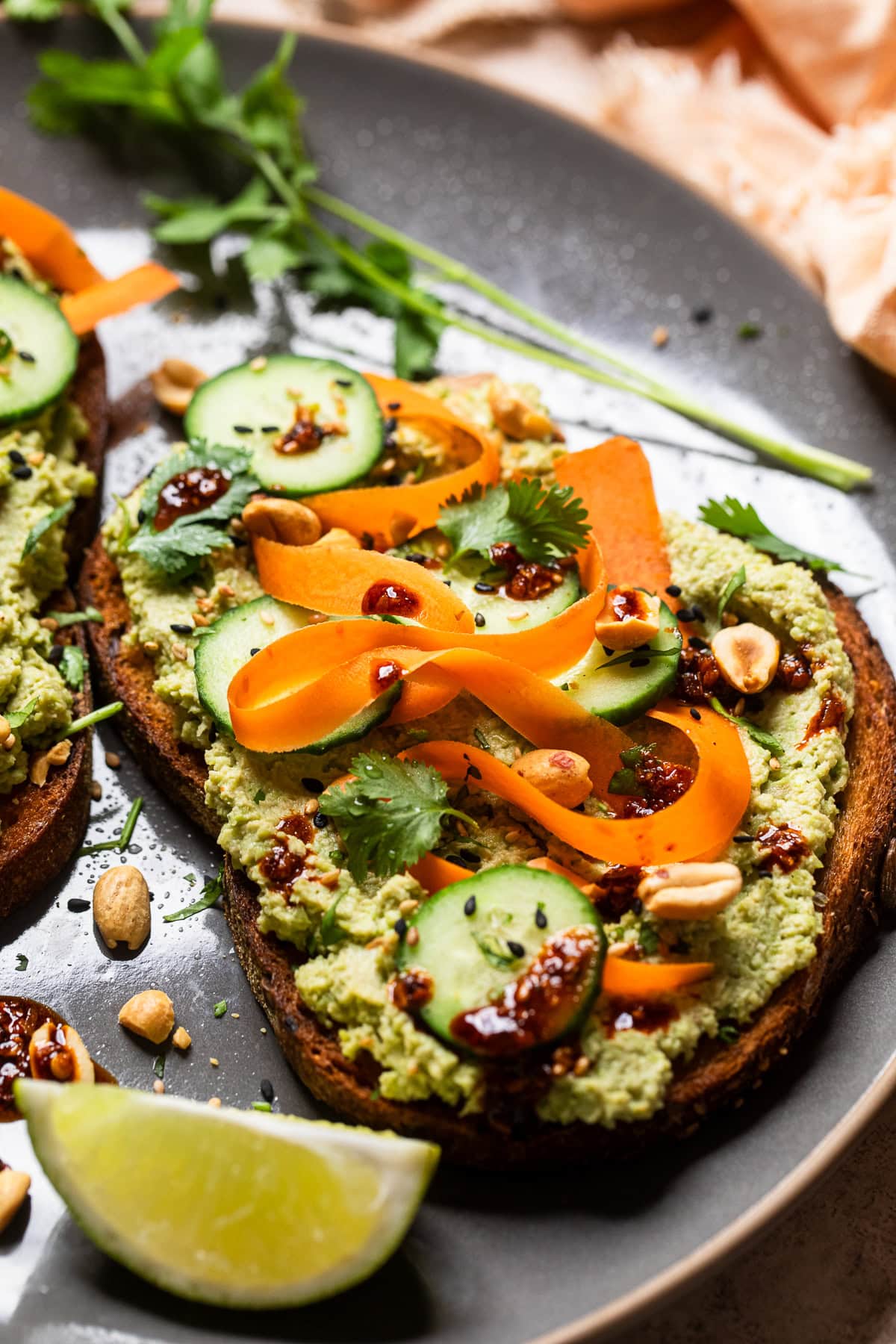 close up of edamame toast with carrot ribbons, sliced baby cucumbers and chili crunch.