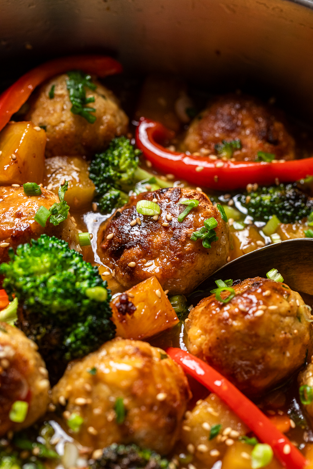 close up of tofu meatballs, red pepper slices, broccoli, and pineapple in a sweet chili sauce.