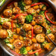 a stainless steel skillet with tofu meatballs, red pepper slices, broccoli, and pineapple in a sweet chili sauce.