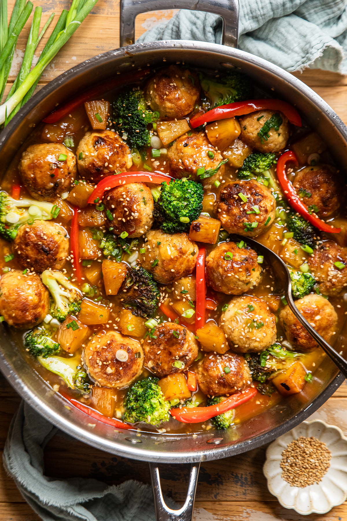 a stainless steel skillet with tofu meatballs, red pepper slices, broccoli, and pineapple in a sweet chili sauce.