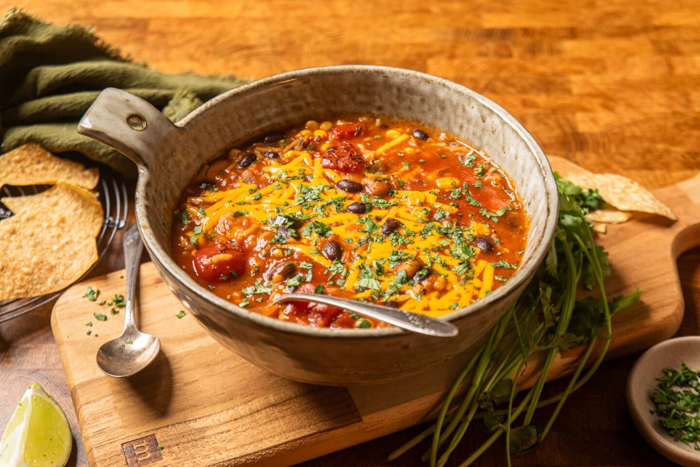 a bowl of enchilada soup topped with green onions and vegan cheddar shreds on a table.