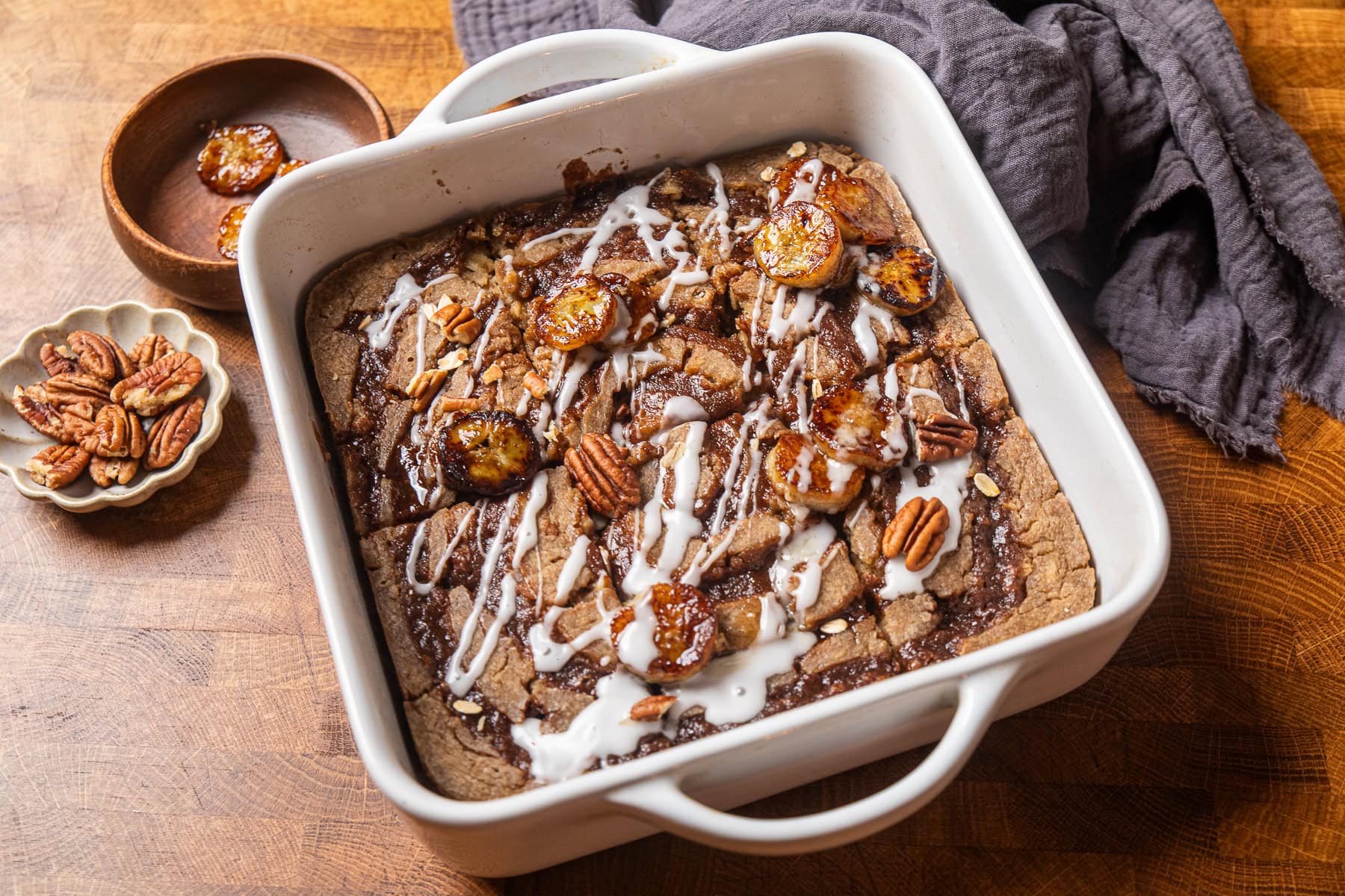 baked cinnamon swirl oatmeal in a white baking dish topped with caramelized bananas and glaze.
