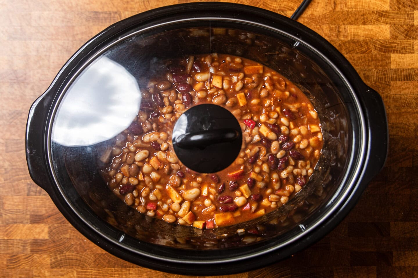 ingredients to make apple cider baked beans in a slow cooker with the lid on.