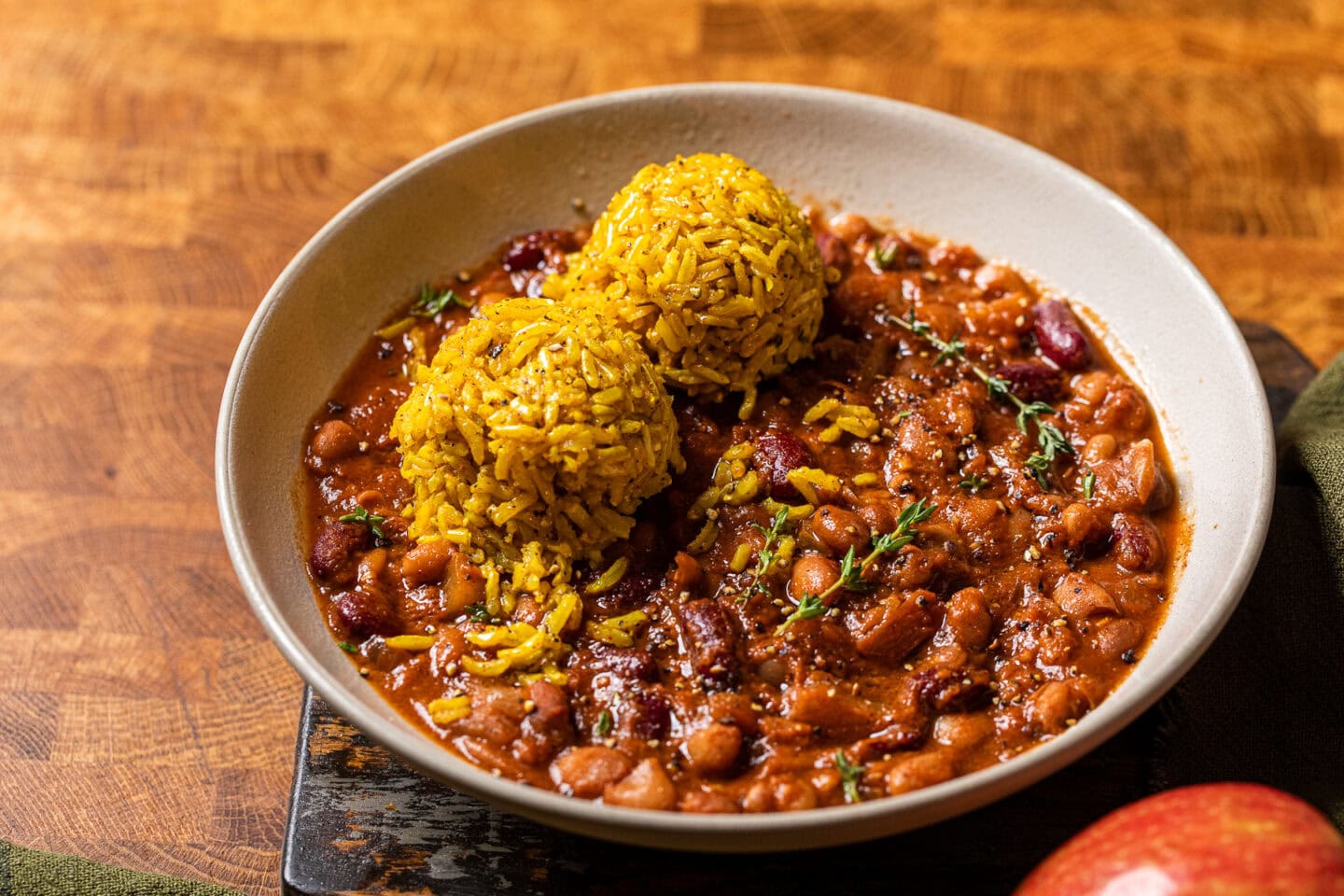 apple cider baked beans in a bowl with a side of two balls of yellow rice.