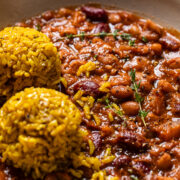 close up of apple cider baked beans in a bowl with a side of two balls of yellow rice.