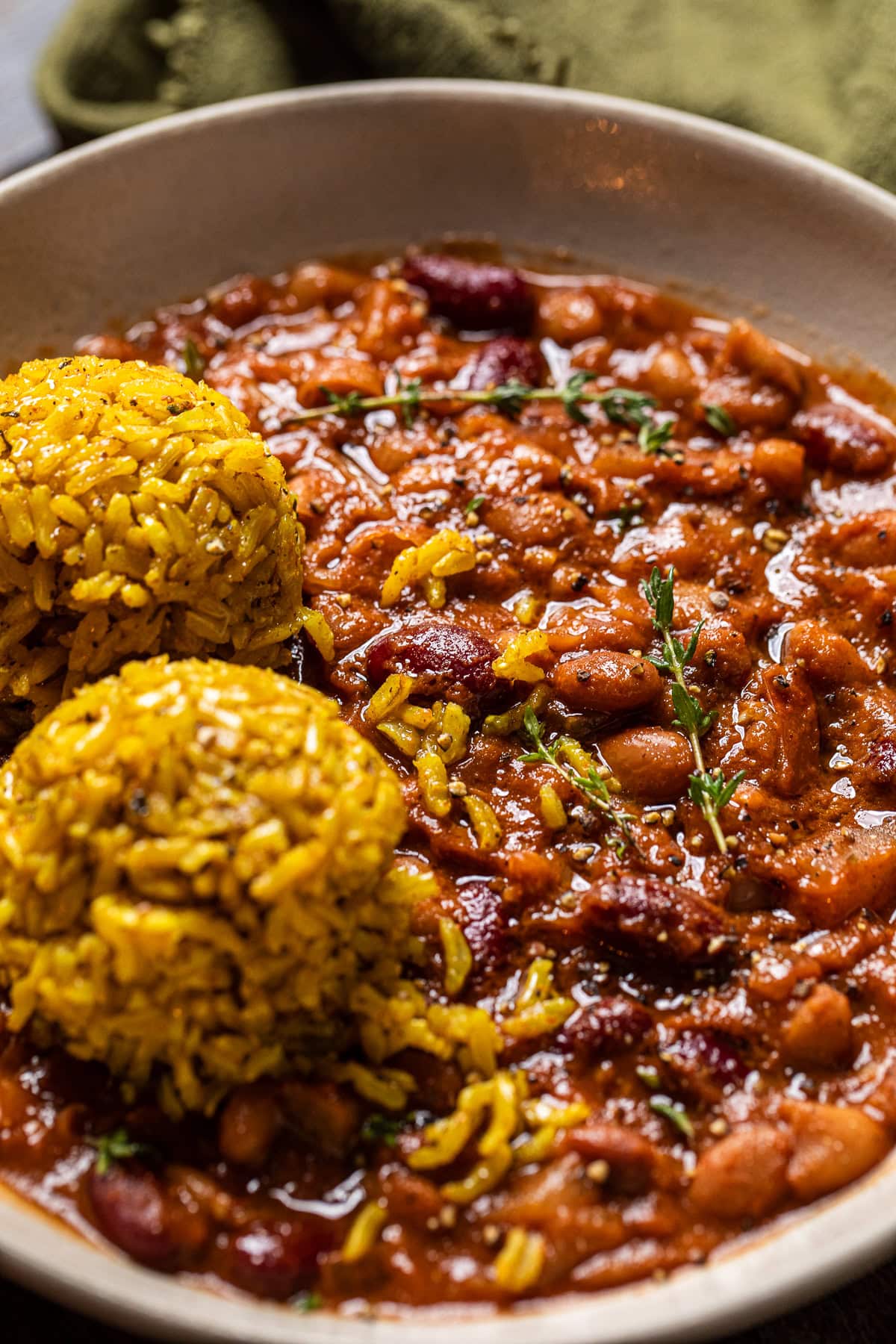 close up of apple cider baked beans in a bowl with a side of two balls of yellow rice.