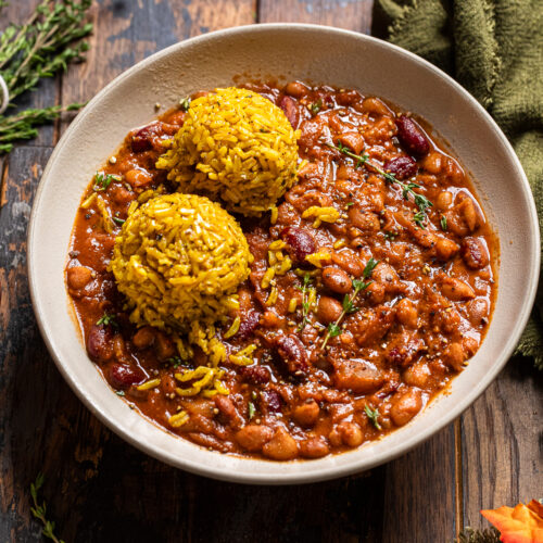 apple cider baked beans in a bowl with a side of two balls of yellow rice.