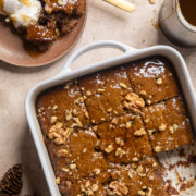 vegan toffee pudding topped with walnuts inside of a square white baking dish next to a plate with some of the pudding and ice cream on it.