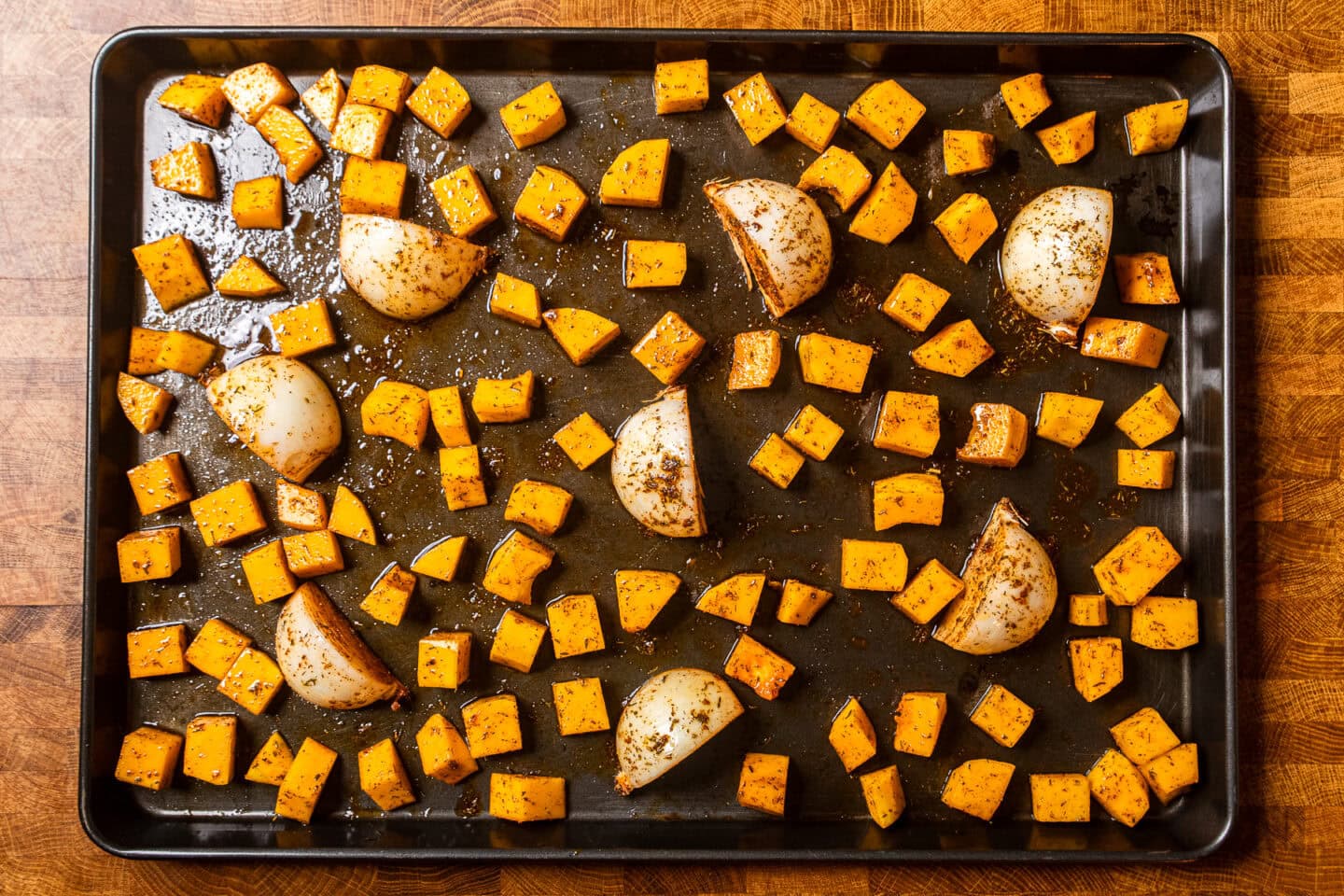 seasoned butternut squash and onion wedges on a sheet pan before being baked.