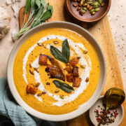 a beige bowl of vegan caramelized onion butternut squash soup topped with sweet potatoes and sage.
