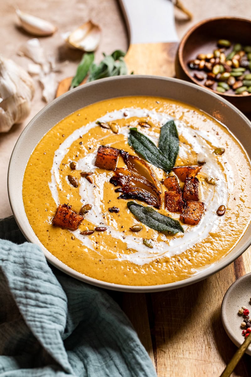 a beige bowl of vegan caramelized onion butternut squash soup topped with sweet potatoes and sage.