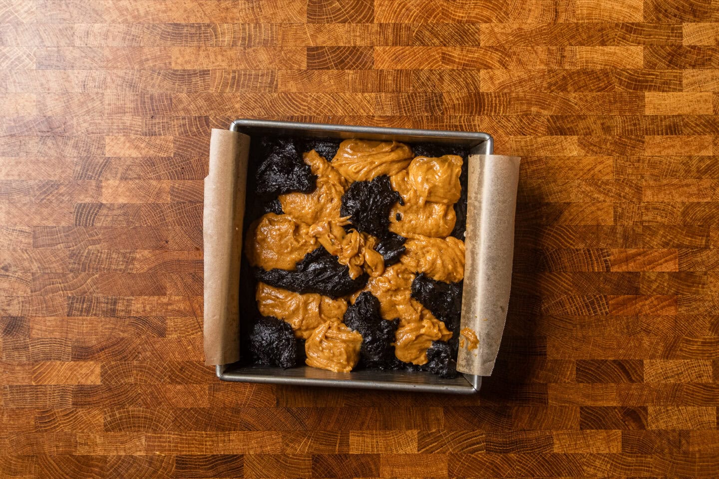uncooked and unswirled pumpkin brownie batters in a baking dish.